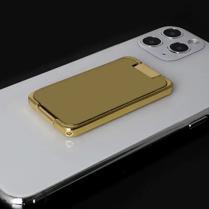 Gold metallic finger ring holder on a silver smartphone with multiple camera lenses